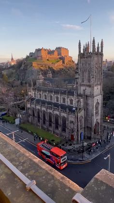 a red double decker bus driving down a street next to a tall building with a castle in the background