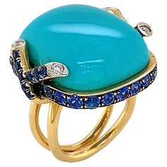 Striking blue of turquoise is the climax of this ring. The polished cabochon is bezel set in 18k yellow gold, which features two inter crossing diamond tipped strands on each side. Sapphires rotate in the bezel setting for a glimmering tranquil accent. Total weights for the gems are 0.14 carats of diamonds, 32.85 carats of turquoise and 3.12 carats of sapphire. The split band complements the setting for a bold finishing touch. Ruby Gold Ring, Yellow Gold Cocktail Ring, Alexis Bittar Jewelry, Cushion Cut Ring, Gold Cocktail Ring, Contemporary Ring, Blue Sapphire Diamond, Cabochon Ring, Celestial Jewelry