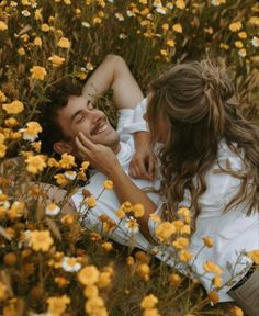 a man and woman laying in a field of flowers with one holding the other's head