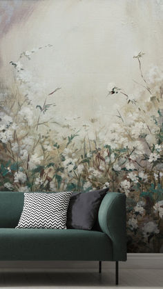 a green couch sitting in front of a wall with flowers on it and a large painting behind it