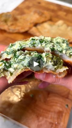 a person is holding up a sandwich with spinach and cheese on it, in front of crackers