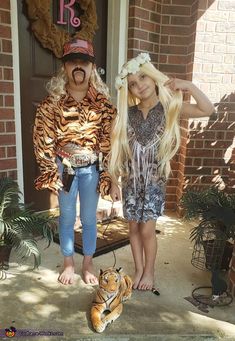 two children in costumes standing on the front porch with a fake tiger laying next to them