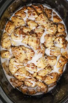 a crock pot filled with cinnamon rolls covered in white icing and sitting on top of a stove