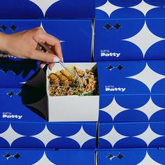 a person holding a fork in a box that is filled with food on top of blue and white boxes