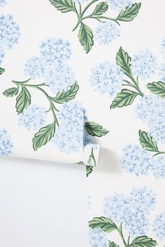 a blue and green floral wallpaper with leaves on the side, next to a roll of white paper