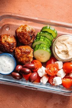 a plastic container filled with meatballs, vegetables and dips on top of a table