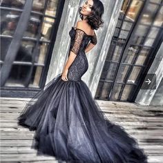 a woman wearing a black dress standing on a wooden floor in front of a building