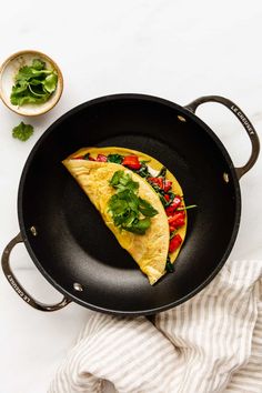 an omelet with spinach and tomatoes in a skillet on a white table