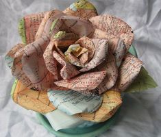 a paper rose is sitting on top of a plate with old map pages around it