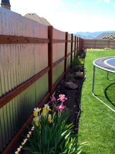 a backyard with a trampoline and flowers in the grass next to a fence