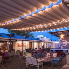 an outdoor seating area with chairs and tables under a covered patio at night, lit by string lights