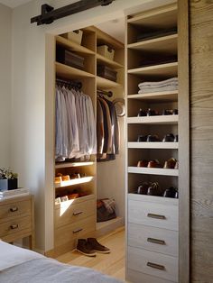 an open closet with clothes and shoes on the shelves next to a bed in a bedroom