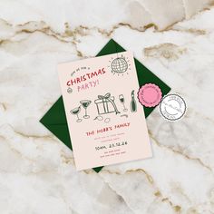 a pink and green christmas party card on top of a marble table with other items