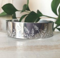 a close up of a metal bracelet on a table with plants and leaves in the background