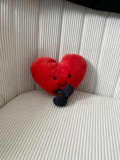 a red heart sitting on the back of a white couch next to a black stuffed animal