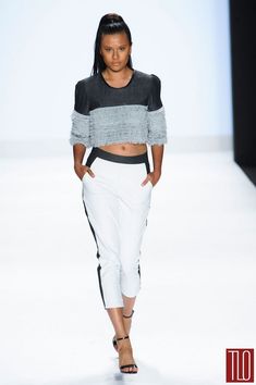 a model walks down the runway wearing white pants and cropped top with black accents