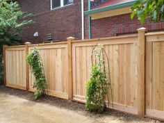 a wooden fence in front of a brick building with green plants growing on the side