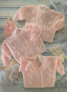 two knitted sweaters, one pink and the other white with buttons on them