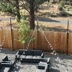 an outdoor seating area with lights strung across the fence and trees in the back ground