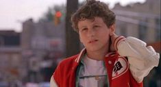 a young boy wearing a red vest and white shirt standing in front of a traffic light