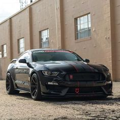 a black mustang parked in front of a brick building with red stripes on it's side