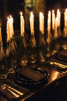 many candles are lit on the table with plates and silverware in front of them