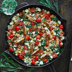 a skillet filled with chicken, tomatoes and corn on top of a wooden table