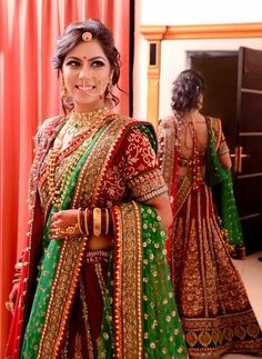 a woman in a green and red bridal outfit standing next to a mirror with her hands on her hips