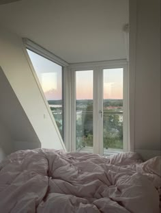 an unmade bed in front of two large windows