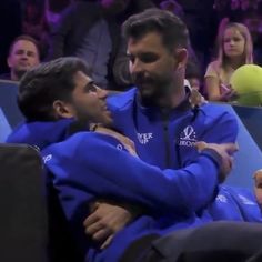 two men in blue jackets hugging each other at a sporting event with people watching from the stands