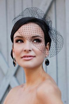 a woman in a wedding dress wearing a birdcage veil over her head and earrings