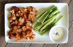 a white plate topped with celery and meat next to a bowl of ranch dressing