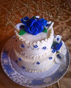 a three tiered cake with blue roses on top and two scissors in the middle