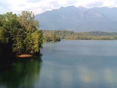 an island in the middle of a lake surrounded by trees and mountains with blue sky