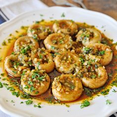 a white plate topped with cooked shrimp covered in sauce and garnished with parsley