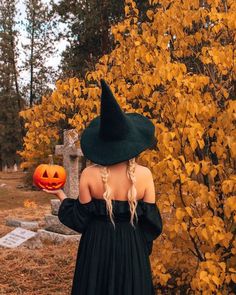 a woman in a black dress and hat holding a pumpkin