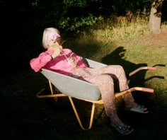 an older woman sitting in a wheelbarrow drinking from a straw cup and looking at her cell phone