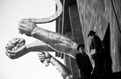 black and white photograph of two men standing in front of a building with a statue