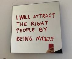 a person holding a cell phone in front of a white board that says i will attract the right people by being myself