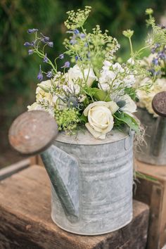 two metal watering cans with flowers in them