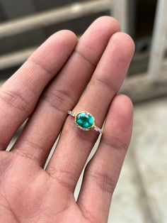 a person's hand holding a ring with an oval shaped green stone on it