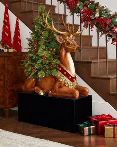 a statue of a deer with a christmas tree on it's back in front of some stairs