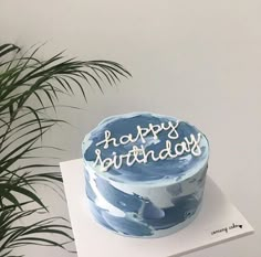 a blue and white birthday cake sitting on top of a table next to a potted plant