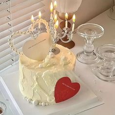 a heart shaped cake sitting on top of a white table next to wine glasses and candles