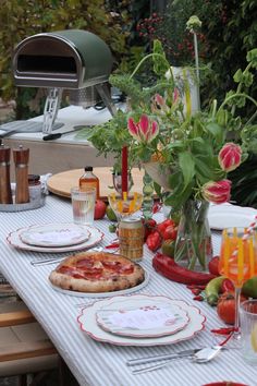 a table set with pizza, flowers and glasses on it for an outdoor dinner party