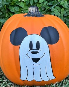 a pumpkin with a ghost face painted on it in front of some grass and bushes