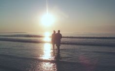 two people are standing in the water at sunset on the beach with their backs to each other