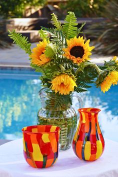 two vases with sunflowers on a table next to a pool