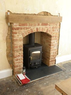 an old brick fireplace with a wood burning stove in the center and some tools on the floor next to it