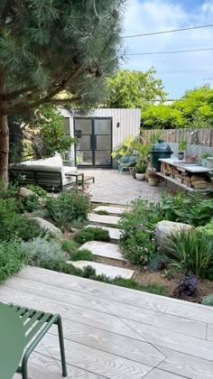 a wooden deck surrounded by green plants and rocks with a small shed in the background